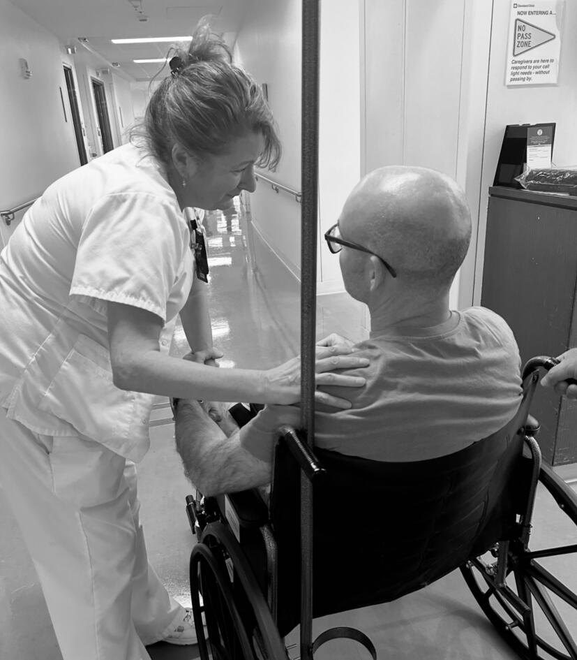 Black-and-white photograph: a nurse steadies John Duffield in a wheelchair in a hospital corridor.