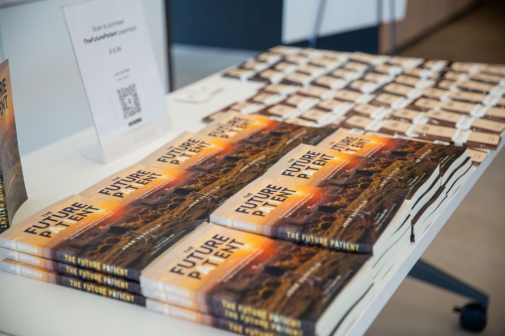 Copies of The Future Patient stacked on a table beside a card with a QR code reading scan to purchase.