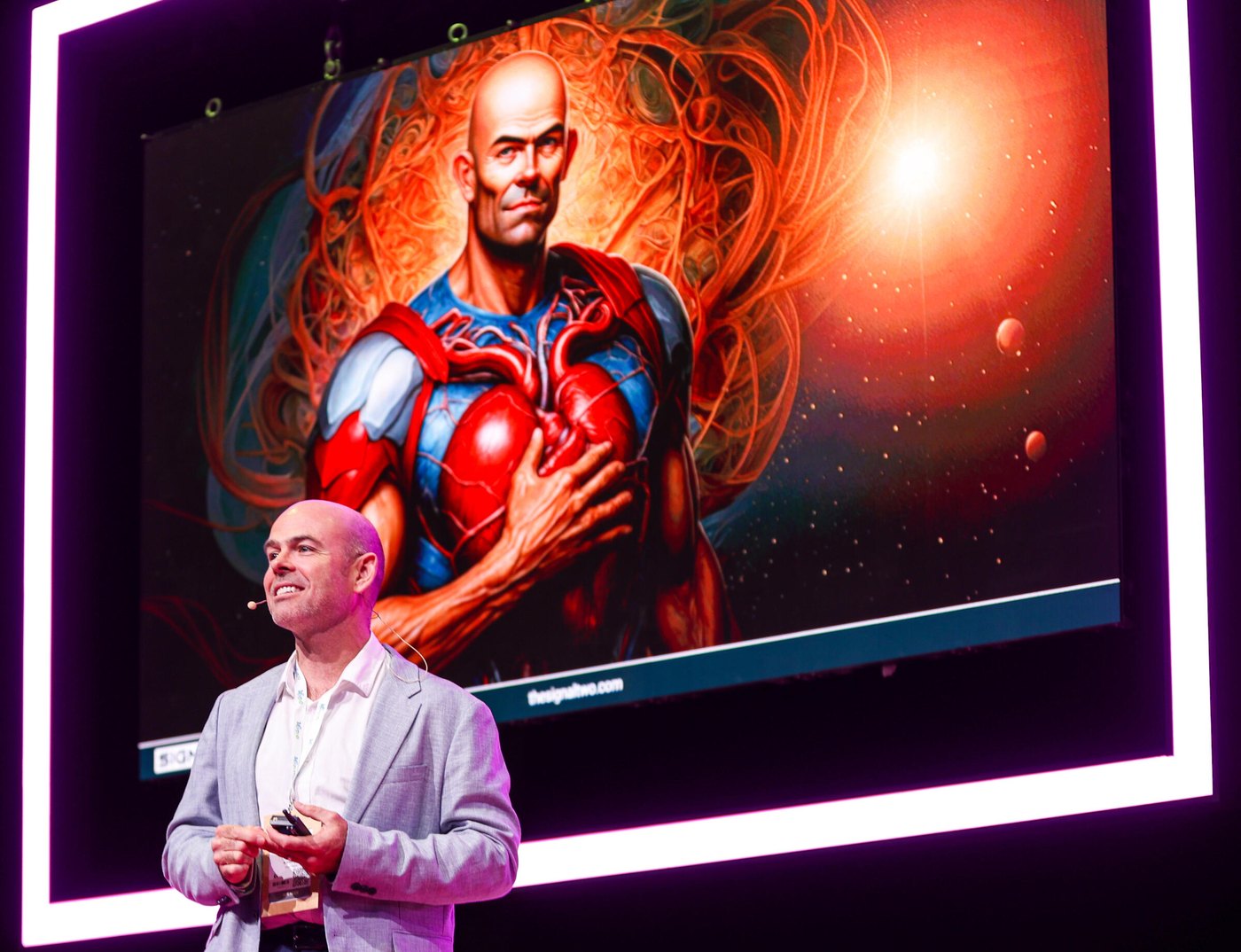 John Duffield on stage in front of a large screen showing an illustration of a human heart wired with light.